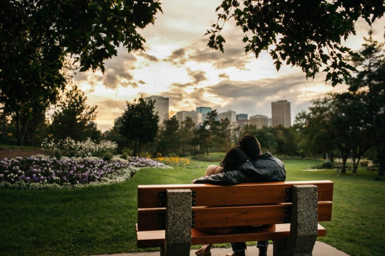 Edmonton Engagement Session at the Muttart Conservatory with the couple sitting on a bench watching a sunset over the cityscape