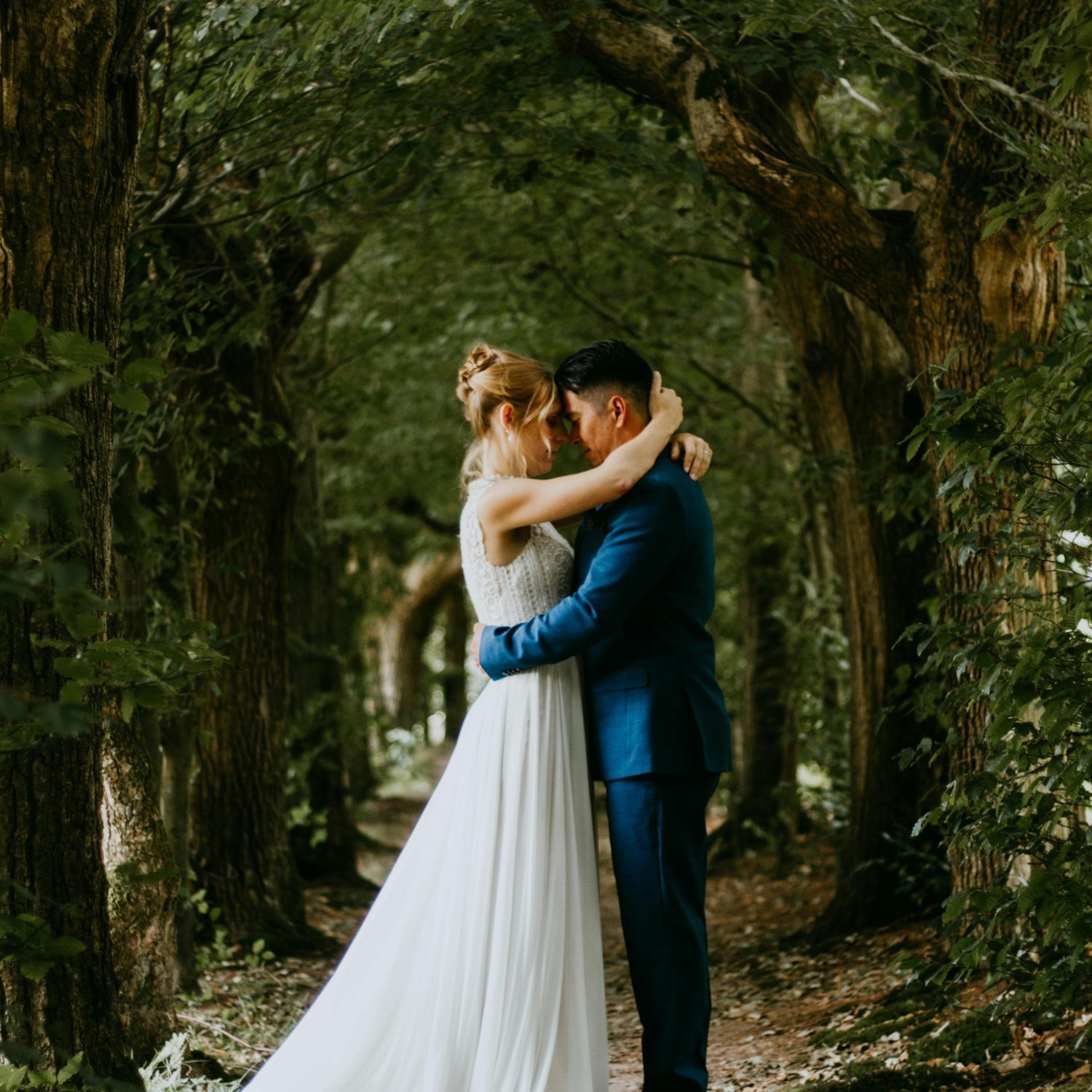 Bride and groom walking through a sun-drenched forest path in Fish Creek Provincial Park