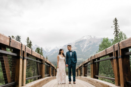 Bride and groom holding hands on a wooden bridge with snowy mountain peaks in the background, a premier Calgary photoshoot location for wedding portraits.